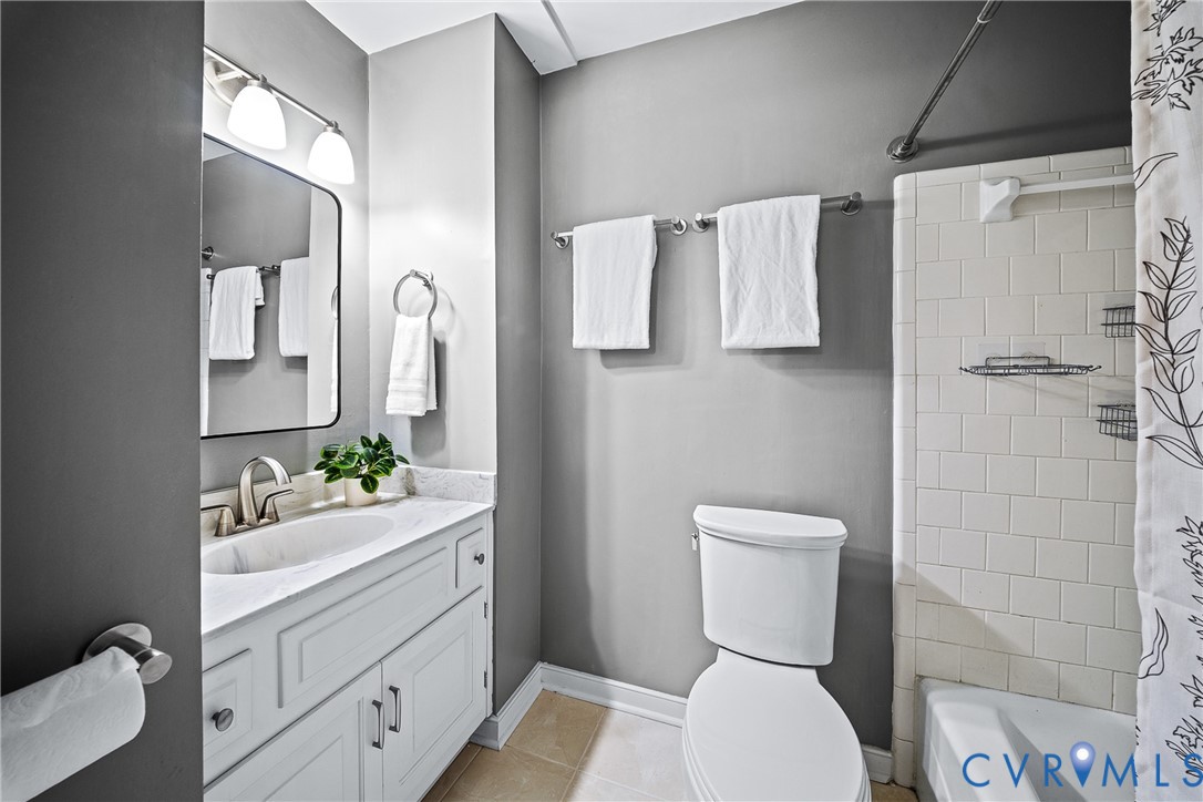 Bathroom featuring a white vanity with stone-style countertop, integrated sink, chrome hardware, rectangular mirror, and tile-surround tub