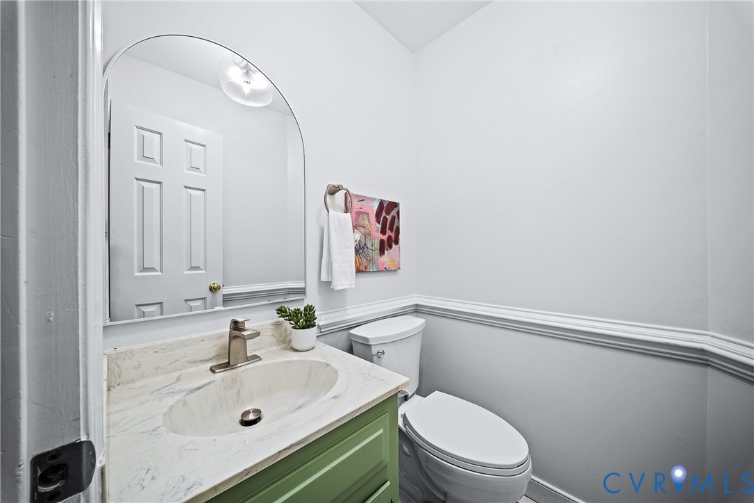 Powder room featuring an arched wall mirror, vanity with a stone-composite countertop, oval undermount sink, brushed-nickel faucet, and chair rail molding
