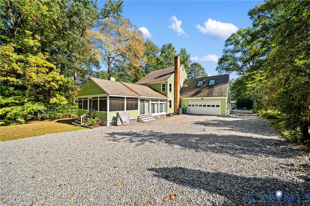 Two-story residence featuring light green siding, an attached two-car garage, a brick chimney, and an expansive screened-in porch, all situated on a gravel driveway Two-story residence featuring light green siding, an attached two-car garage, a brick chimney, and an expansive screened-in porch, all situated on a gravel driveway
