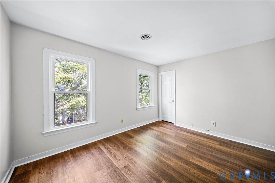 Interior room featuring wood-finish flooring, two double-hung windows, and a six-panel interior door