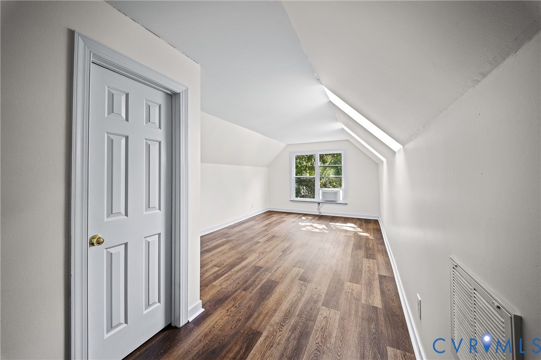 Interior space featuring wood-finish flooring, vaulted ceilings, and a single-panel recessed door