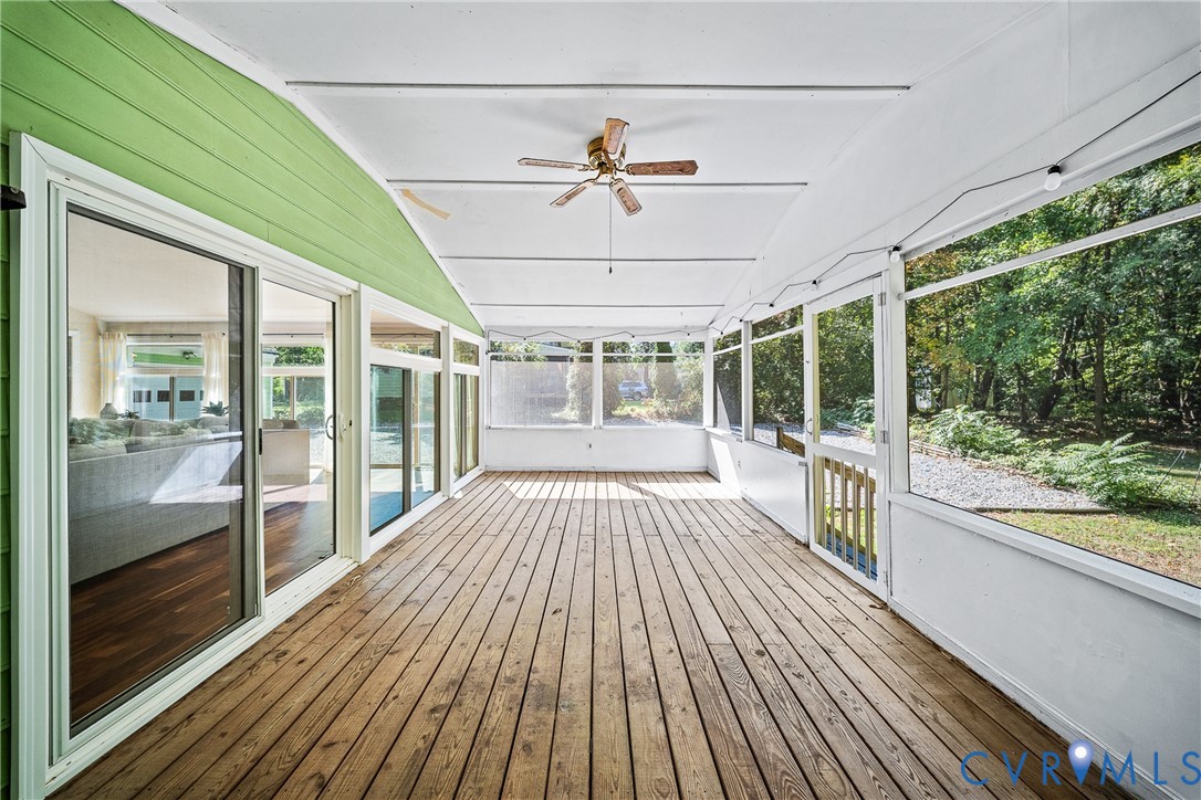 Enclosed porch featuring wood decking, floor-to-ceiling screen panels, a ceiling fan, and sliding glass entry doors