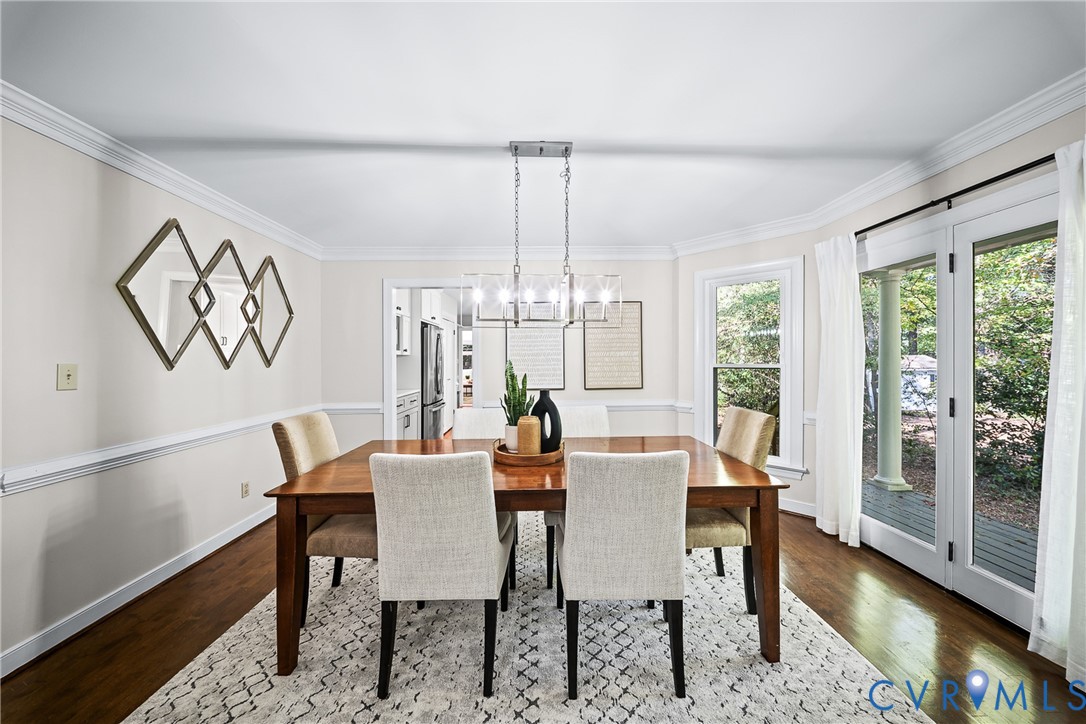 Dining space featuring wood-finish flooring, crown molding, chair rail trim, a contemporary linear chandelier, and double glass doors providing exterior access