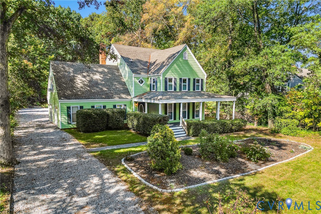 Two-story home with light green horizontal lap siding, covered front porch, gravel driveway, and mature landscaping