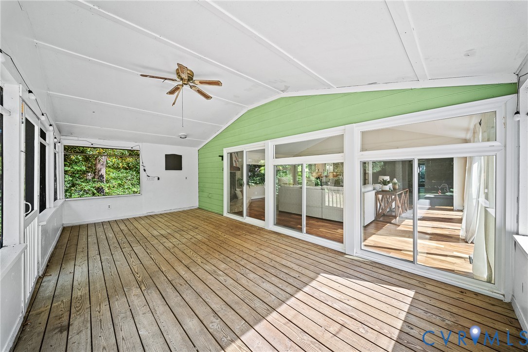 Enclosed porch featuring wood decking, vaulted ceiling, ceiling fan, and extensive sliding glass wall panels