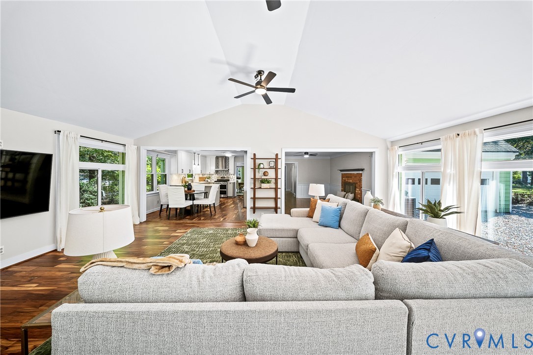 Vaulted ceiling with a central blade-style ceiling fan, wood-finish flooring, and expansive windows