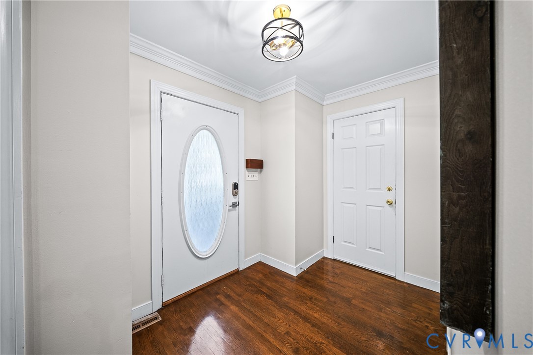 Entryway featuring wood-finish flooring, crown molding, a decorative orb chandelier, and a solid-core door with an oval glass insert