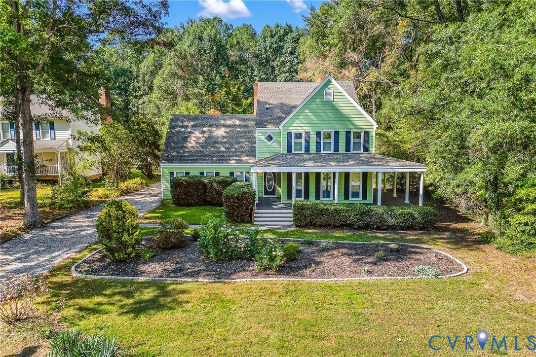Two-story home with lap siding, a covered front porch, multi-pane windows, a pitched shingled roof, and stone-edged landscaping beds