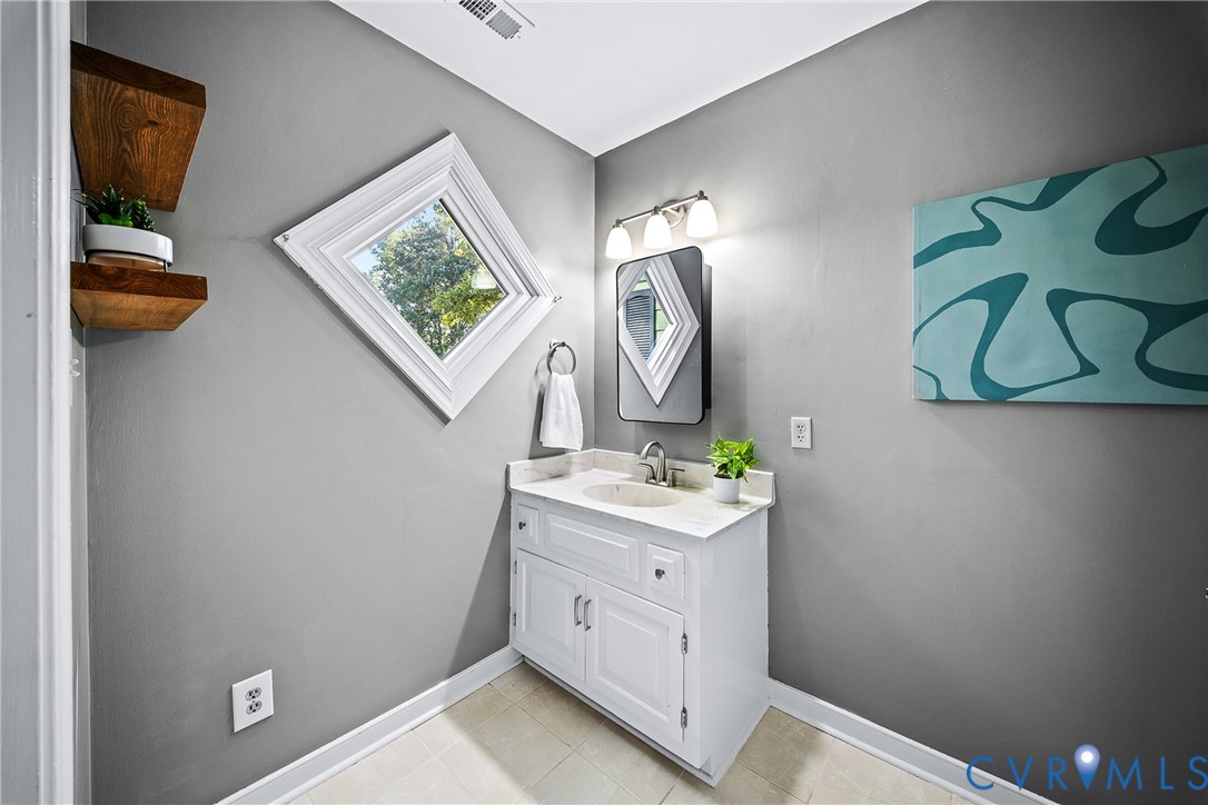 White vanity with a stone countertop, integrated oval sink, diamond-shaped window, three-light fixture, and wall-mounted wooden shelving