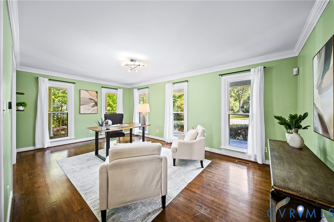 Spacious room featuring wood-finish flooring, crown molding, and multiple tall windows providing abundant natural light