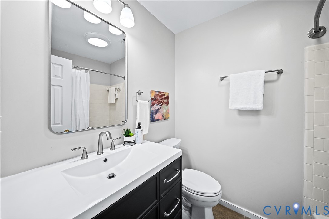 Bathroom featuring a vanity with dark cabinetry and a white integrated sink, polished metal faucet, rectangular mirror with rounded corners, and a tiled shower surround
