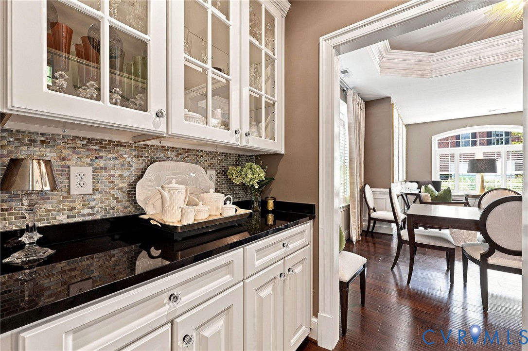 White cabinetry with glass-front uppers, dark countertops, and a mosaic tile backsplash