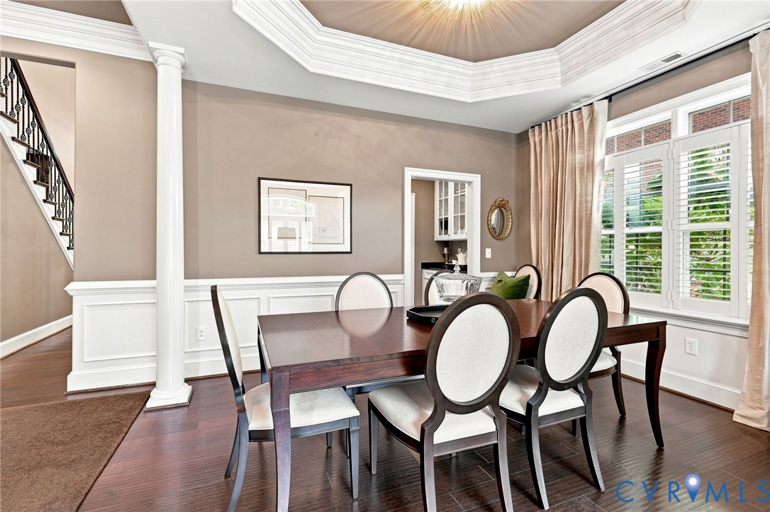 Hardwood flooring, decorative wainscoting, and an ornate tray ceiling with crown molding