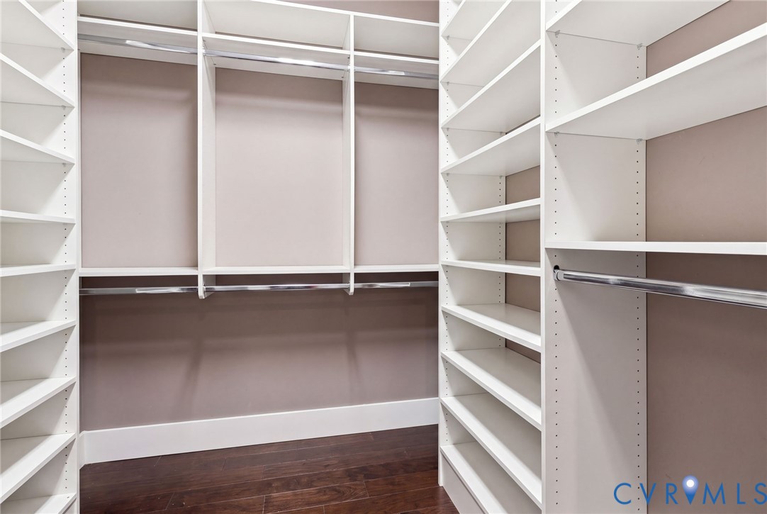 Built-in closet system featuring white shelving, multiple hanging rods, and dark wood-finish flooring