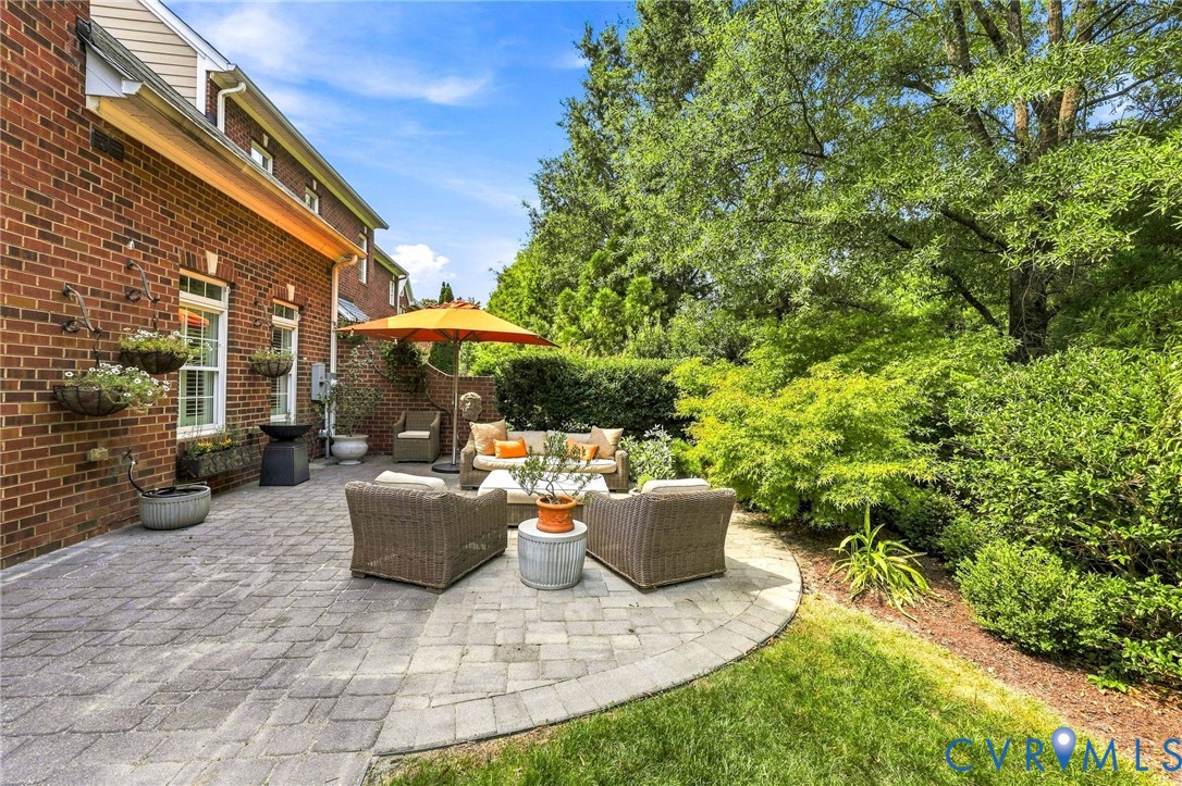 Garden patio living with brick exterior, huge extended stone paver patio, lush landscaping, brick side privacy wall, and gas plumbed for outdoor grill or firepit.
