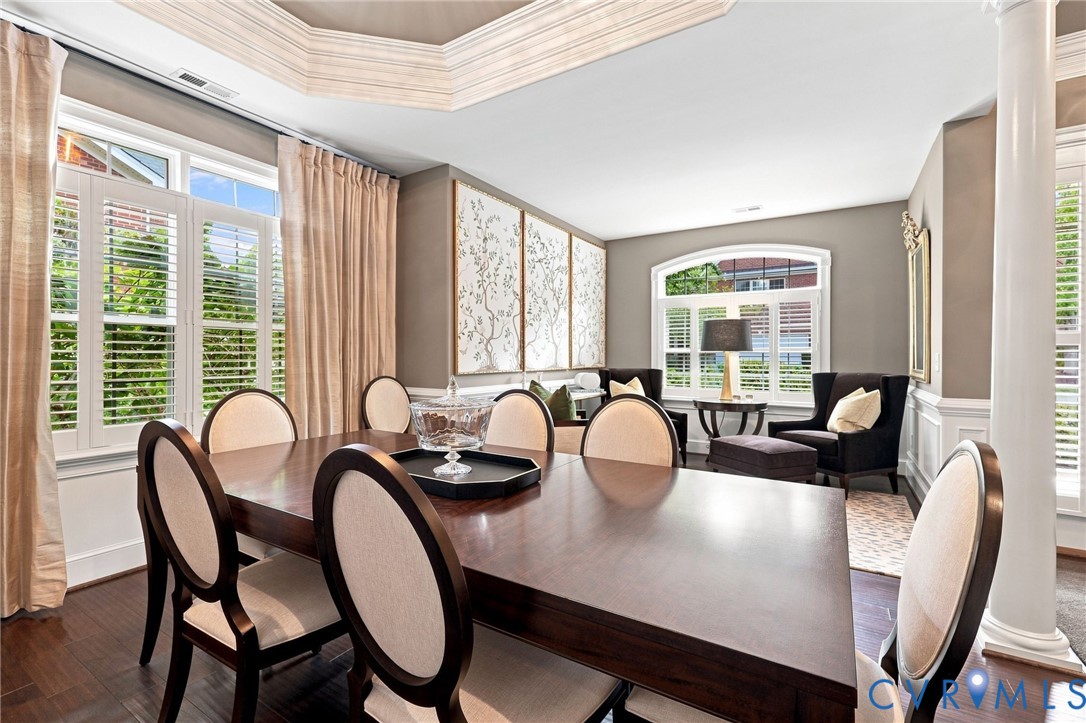 Coffered ceiling, wood-finish flooring, white plantation shutters, decorative wall paneling, and a large arched window