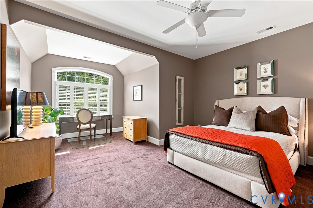 2nd ensuite primary bedroom on level 2, with arched window (with shutters and solar film), 9' ceilings, ceiling fan/light, and carpet flooring