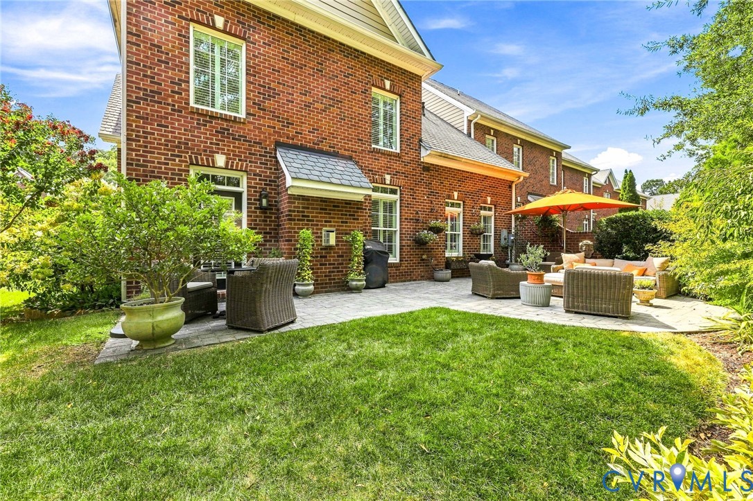 Brick exterior with extended paver patio, lush landscaping, and brick side privacy wall