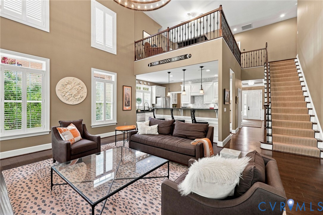 Two-story living area with dark wood-finish flooring, white plantation shutters, and a prominent staircase with carpeted treads