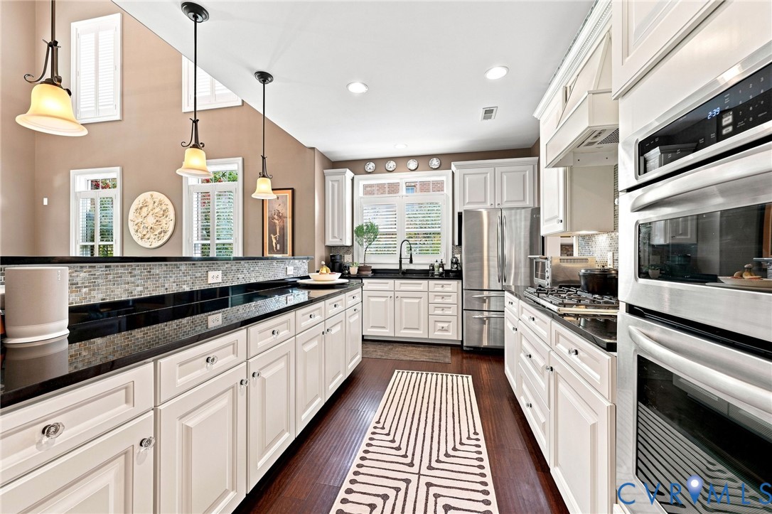 Kitchen featuring white cabinetry, dark countertops, a mosaic tile backsplash, stainless steel appliances, and wood-finish flooring
