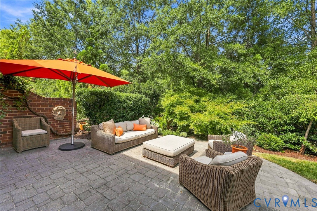 Brick paver patio, brick retaining wall, mature perimeter landscaping, and decorative wall-mounted sculptural element