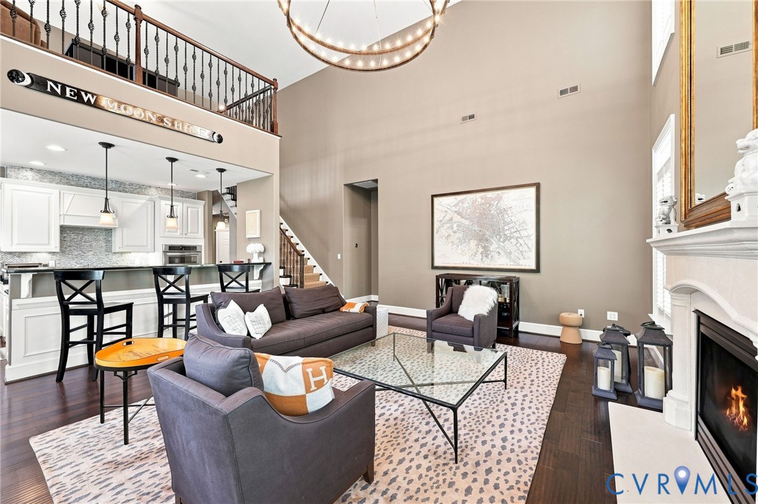 Vaulted ceiling with an illuminated circular fixture, dark wood-finish flooring, white fireplace with hearth, and a kitchen bar with pendant lighting