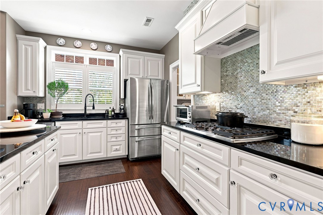 White cabinetry with dark contrasting countertops, a stainless steel French door refrigerator, and a gas range with a dedicated vent hood