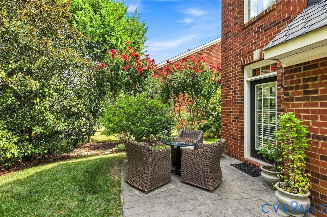 Brick exterior with a paved patio, a black framed door with glass panels, and mature landscaping with red flowering shrubs