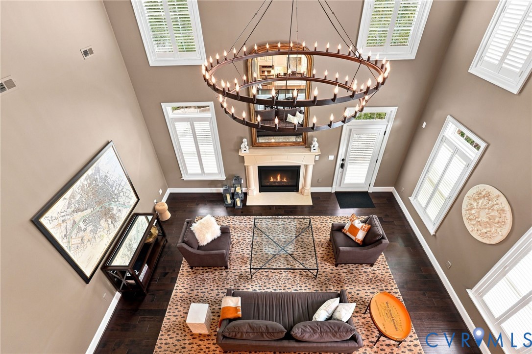 Two-story living area featuring a large chandelier, wood-finish flooring, a fireplace with a mantel, multiple windows, and a glass-paneled door