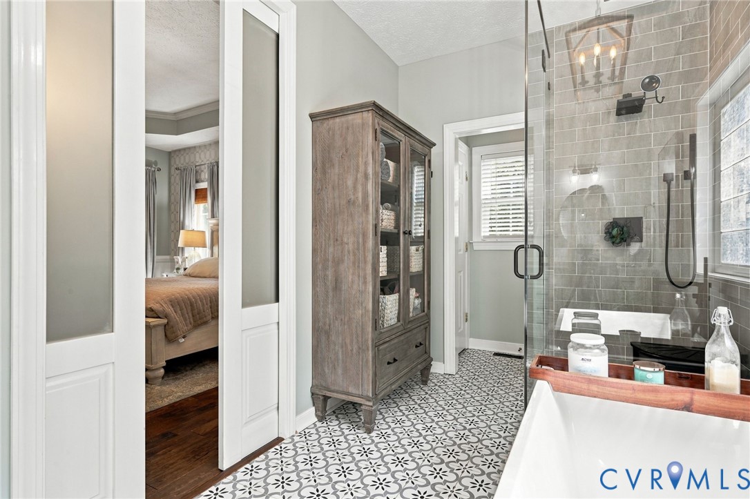 Patterned floor tiling, glass-enclosed shower, subway tile shower surround, freestanding soaking tub, wood-finish storage cabinet