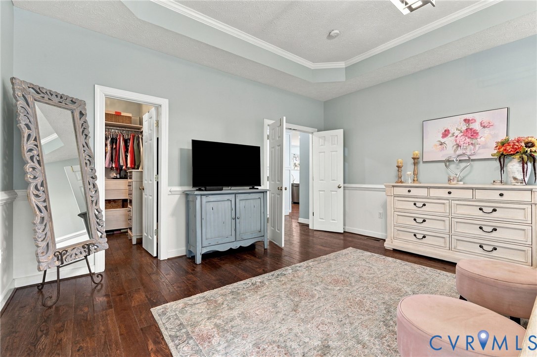 Tray ceiling with crown molding, light blue wall paint, chair rail molding, dark wood-finish flooring, and a walk-in closet with built-in shelving