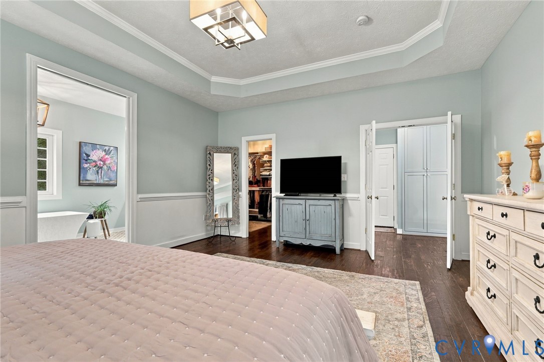 Tray ceiling with crown molding, wood-finish flooring, half wall paneling, built-in storage cabinetry, and an interior doorway leading to an additional space