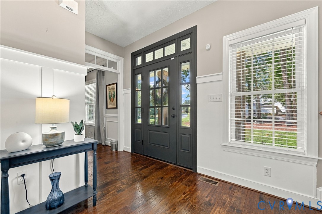 Hardwood flooring, dark-toned double entry doors with glass panels, a transom window, wainscoting, and a white-framed window
