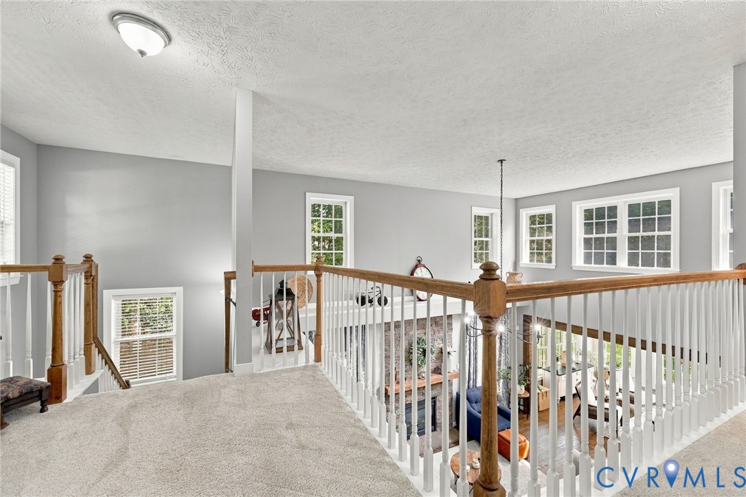 Carpeted landing featuring a wood and white spindle railing, multiple windows with white trim, and light gray wall finishes