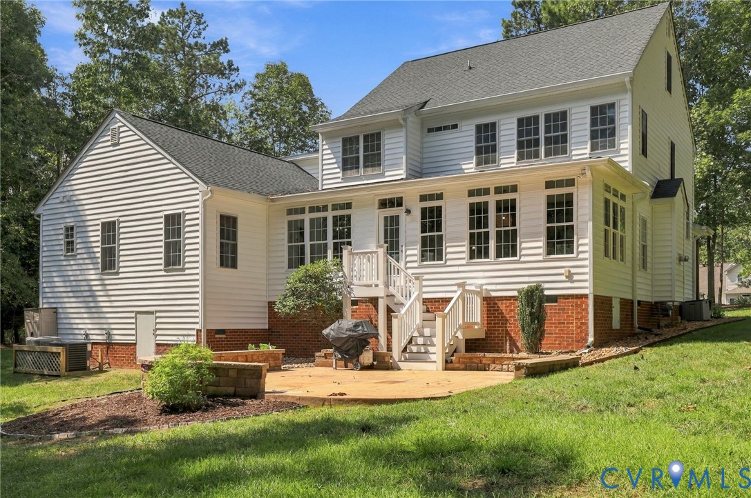 White siding exterior with a dark shingle roof, a ground-level patio, and a tiered deck