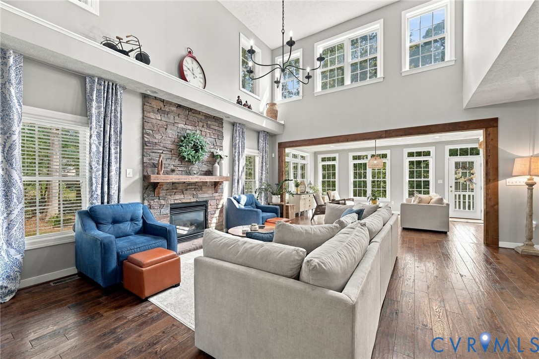 Two-story living area featuring a stone fireplace with a wood mantle, hardwood flooring, and multiple large windows