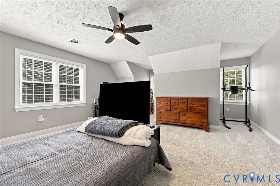Neutral toned walls, soft carpet flooring, white trim windows, and a ceiling fan with integrated lighting
