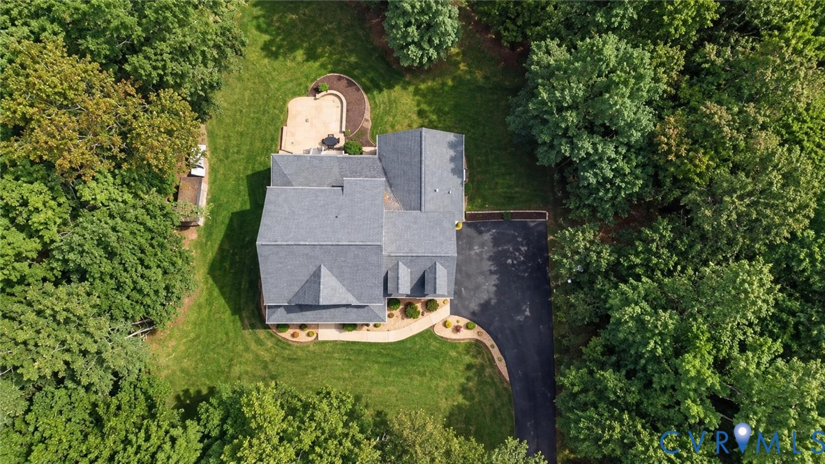 Expansive property featuring a grey shingle roof, paved driveway, mature trees, and a stone patio