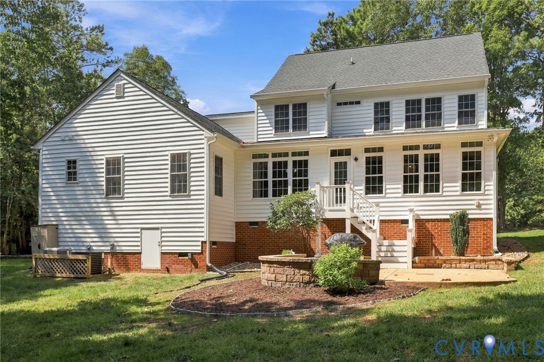 Rear exterior featuring white siding, a multi-pane window array, and a stone-accented patio with a built-in fire pit
