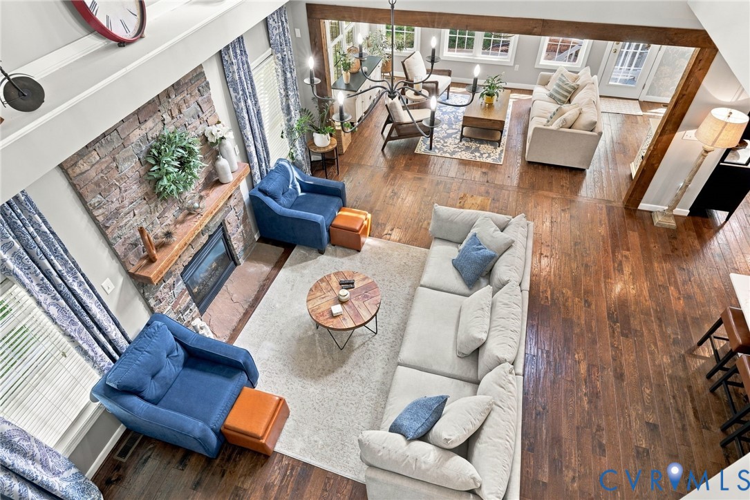 Great room featuring wood-finish flooring, a stone fireplace with a wood mantel, and exposed wood beams