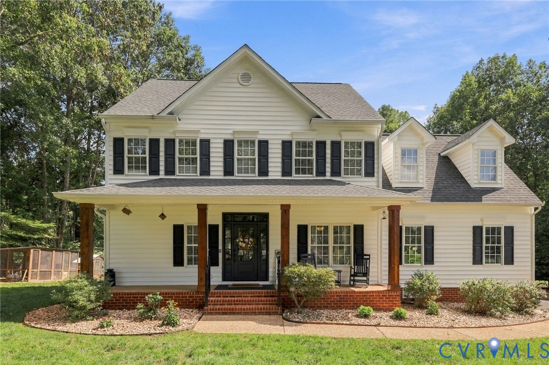 Siding exterior with multiple dormers, covered front porch with wood-finish columns, brick foundation, and dark window shutters