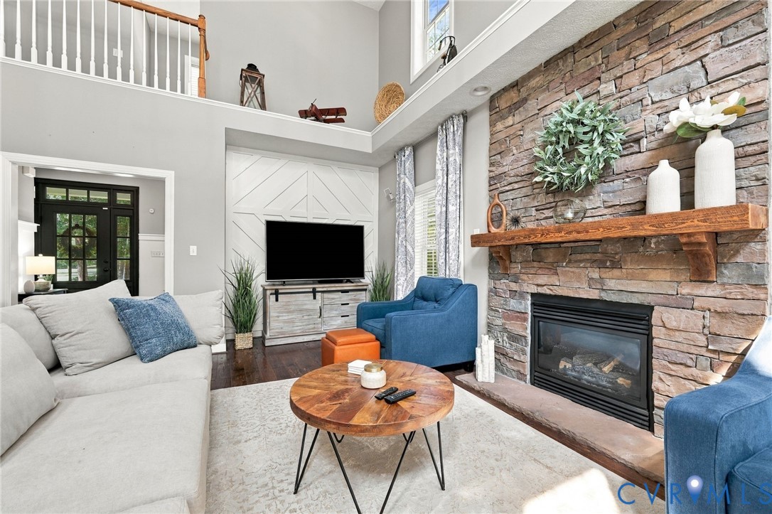 Stone-faced fireplace with a wood mantel, wood-finish flooring, and a two-story ceiling