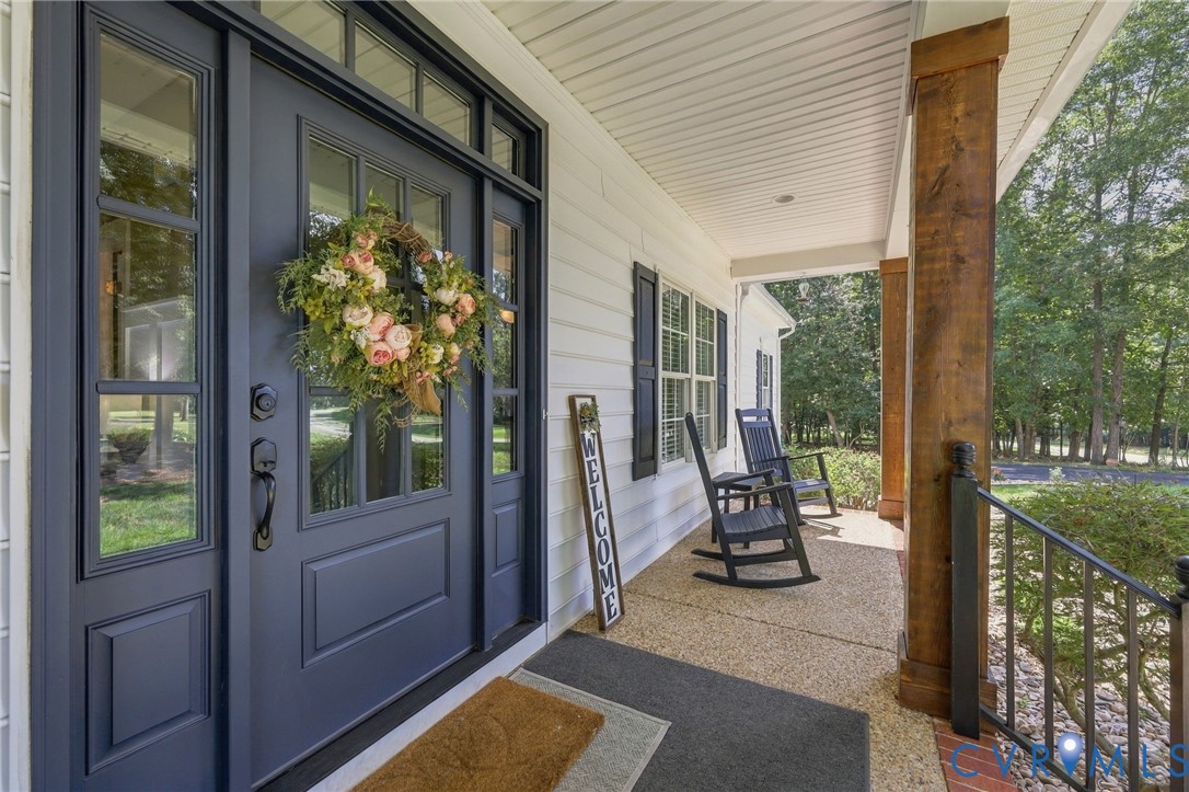 Welcoming front porch featuring a dark paneled entry door with sidelights, durable vinyl siding, exposed wood support columns, and an aggregate concrete surface