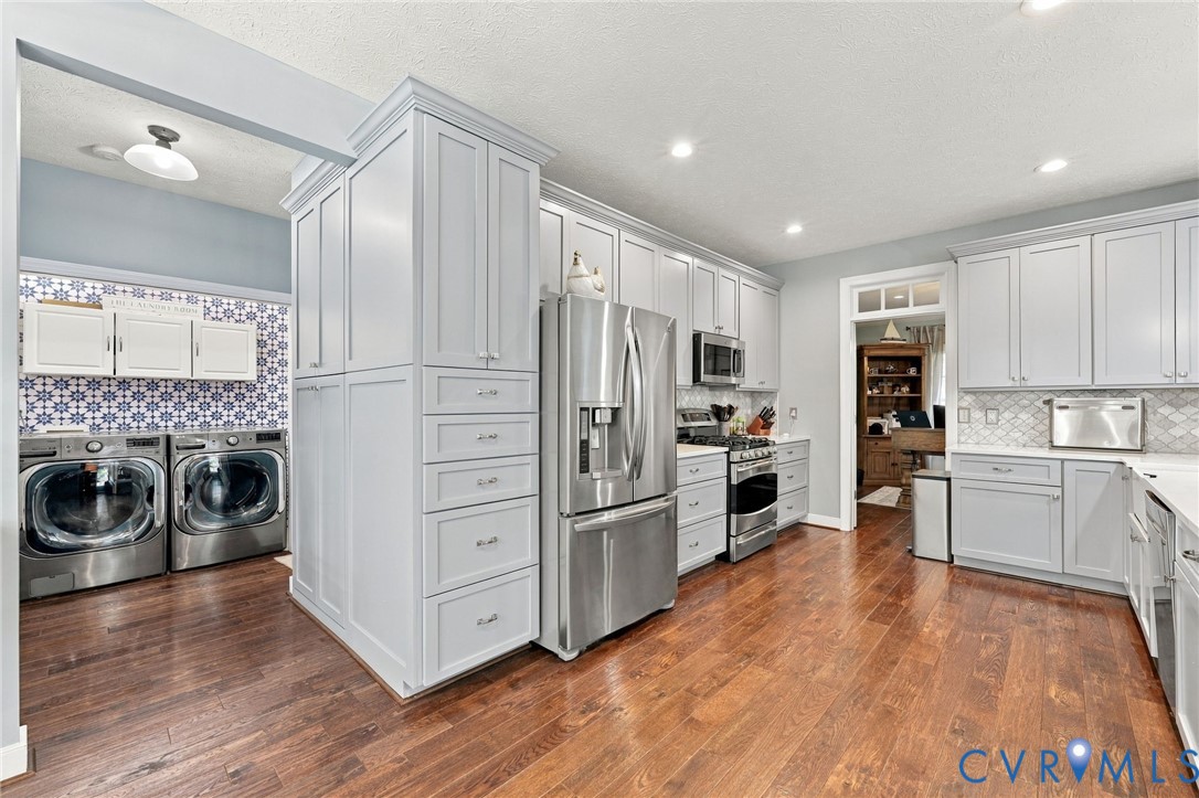 Wood-finish flooring, recessed lighting, light-toned cabinetry, stainless steel appliances, and patterned tile backsplash