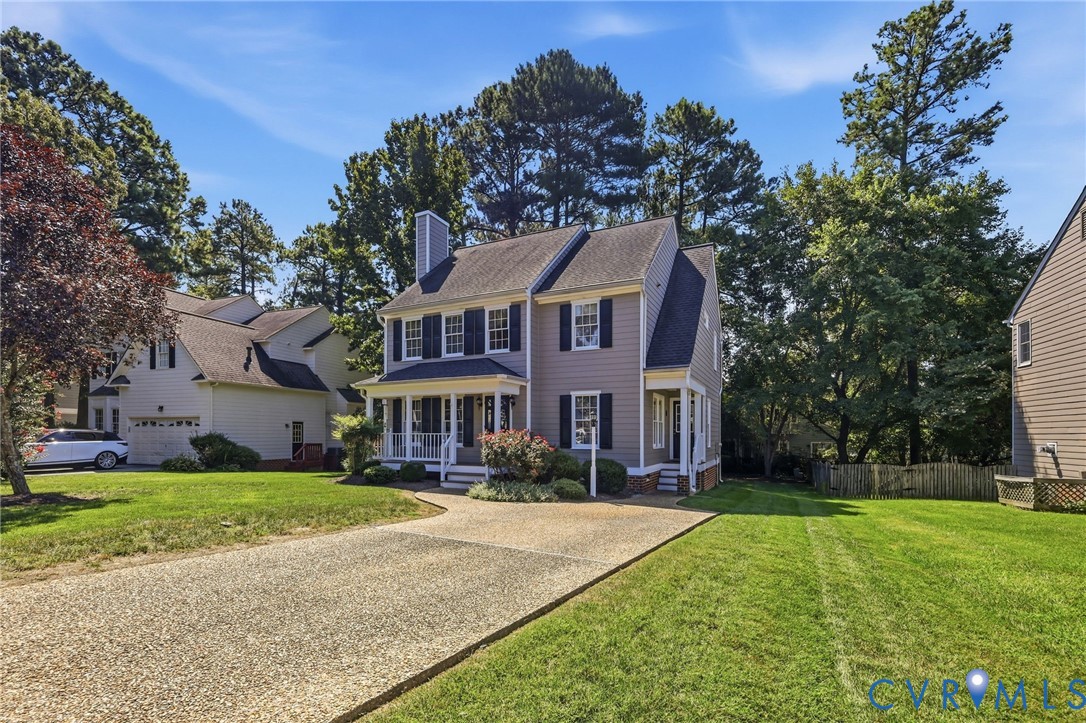 Traditional-style residence with a covered porch, dormer windows, and a gravel driveway