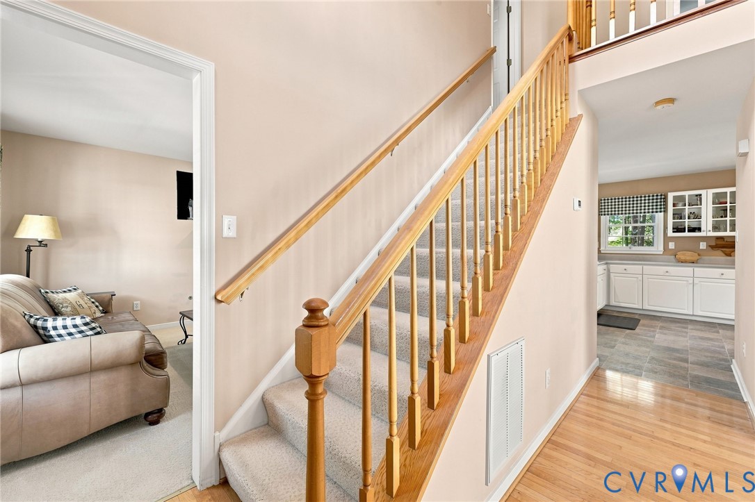 Hardwood flooring, carpeted staircase with wood banister, and a kitchen featuring white cabinetry and a window