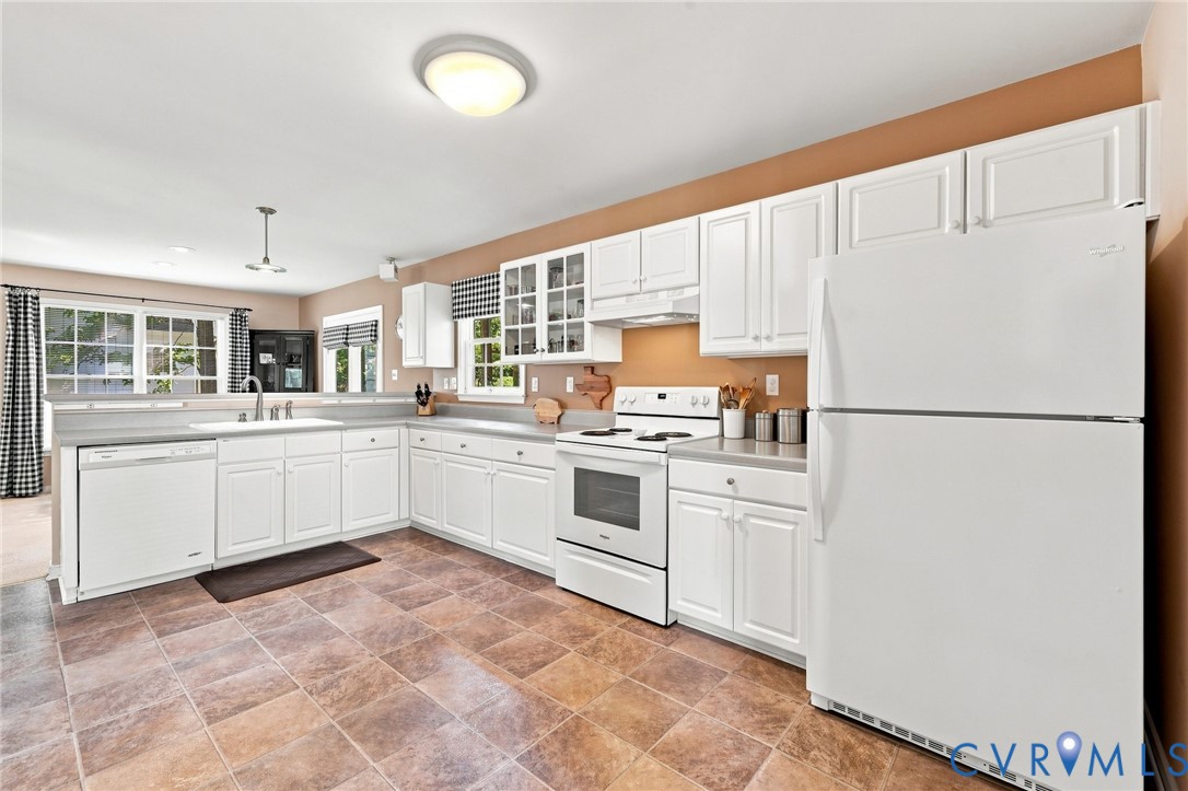 Spacious kitchen featuring white cabinetry with glass-front upper cabinets, stainless steel appliances including a double-door refrigerator and electric range, laminate countertops, an undermount sink with chrome fixtures, and stone-finish flooring throughout