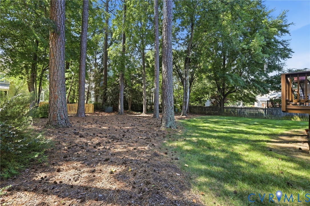 Expansive backyard featuring mature trees, a manicured lawn, and a wooden privacy fence