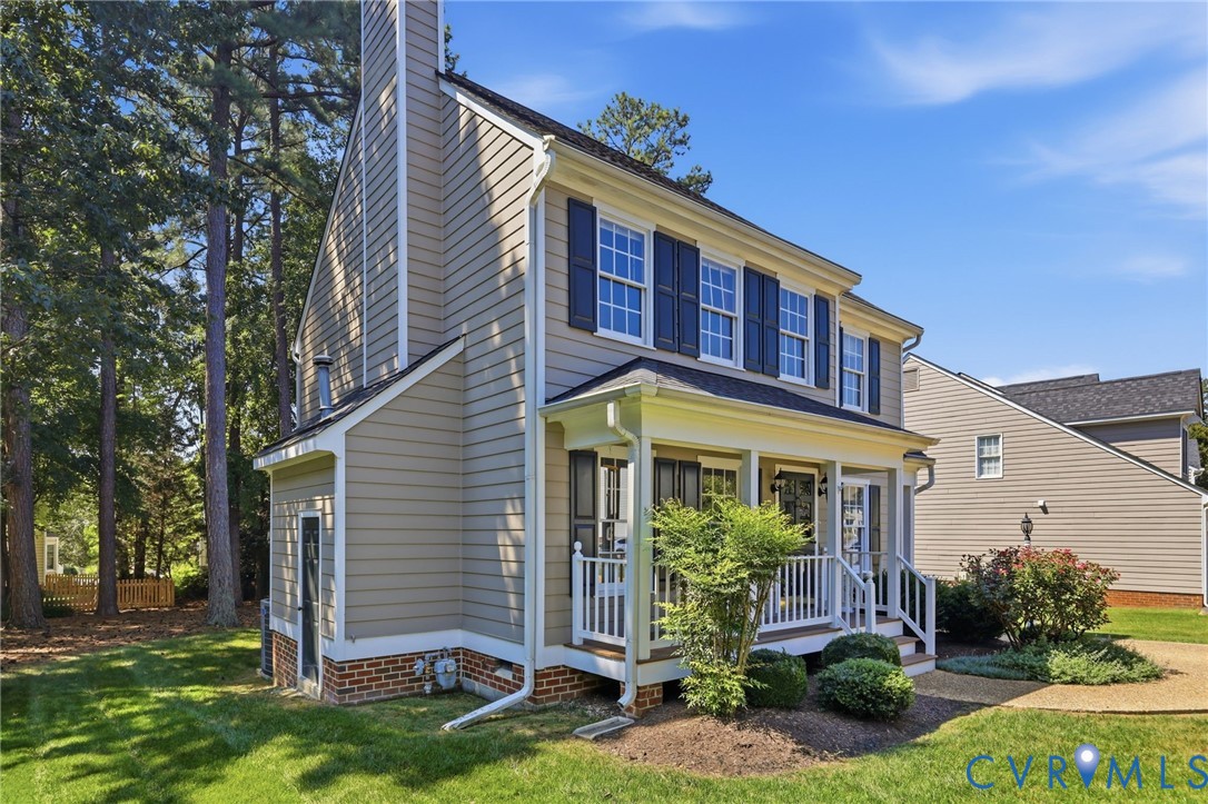 Two-story residence featuring light-toned siding, dark shutters, a covered front porch, and a prominent chimney