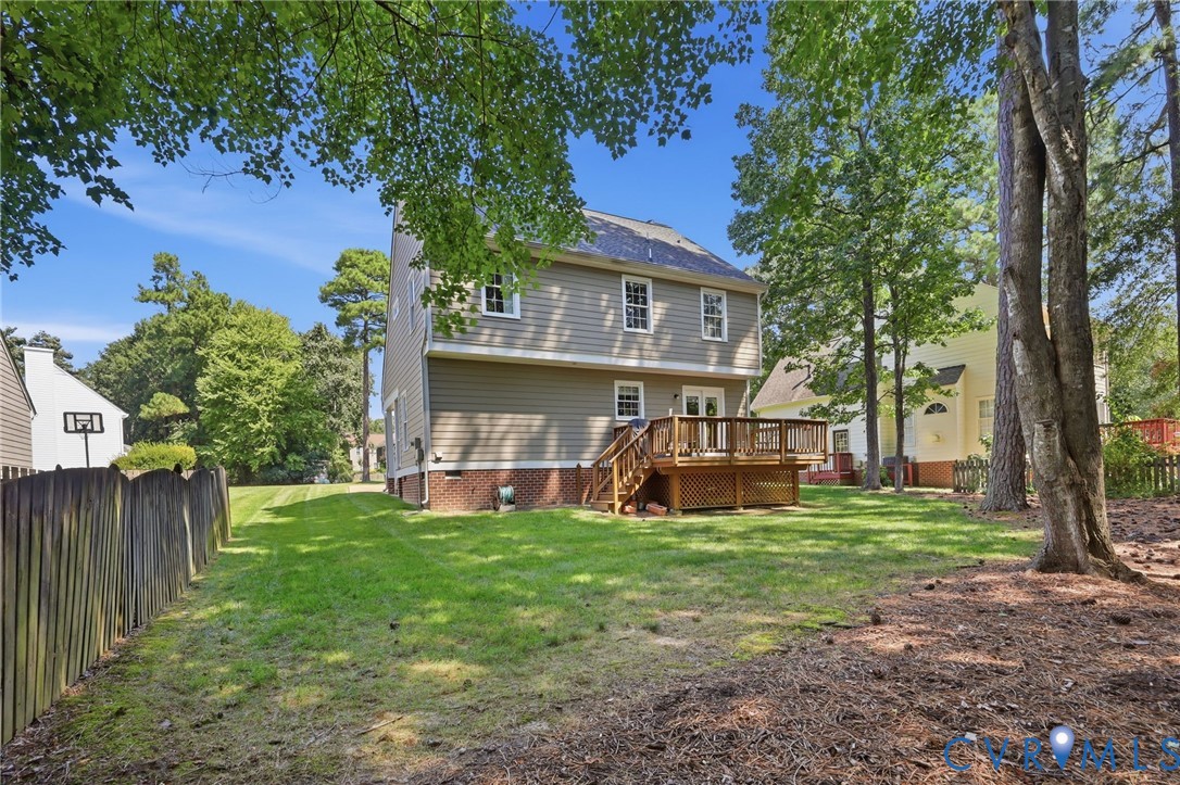 Expansive backyard featuring a manicured lawn, a multi-level wood deck, a wood privacy fence, mature trees, and a two-story exterior with siding